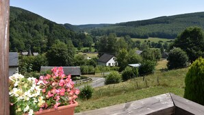 A rural landscape with a wooden deck, a white house, and a flower pot with pink and white flowers. - Scandinavian chalet, warm atmosphere, for those who love nature (Lierneux)