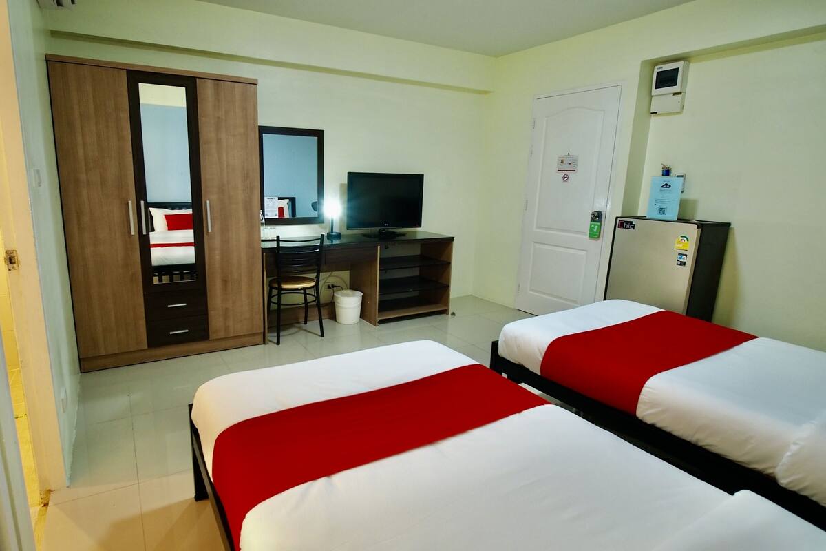 Hotellihuone, jossa on kaksi erillistä sänkyä, työpöytä tietokoneella, vaatekaappi, peili, televisio, jääkaappi ja ovi, jossa on turvalukko.