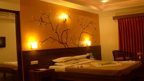 Habitación de hotel con cama, escritorio, silla, televisor y un mural de un árbol en la pared.