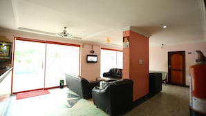 Una sala de estar con un sofá, una mesa de centro y un televisor. Se observa una puerta que da a otra habitación y un extintor rojo en el suelo.