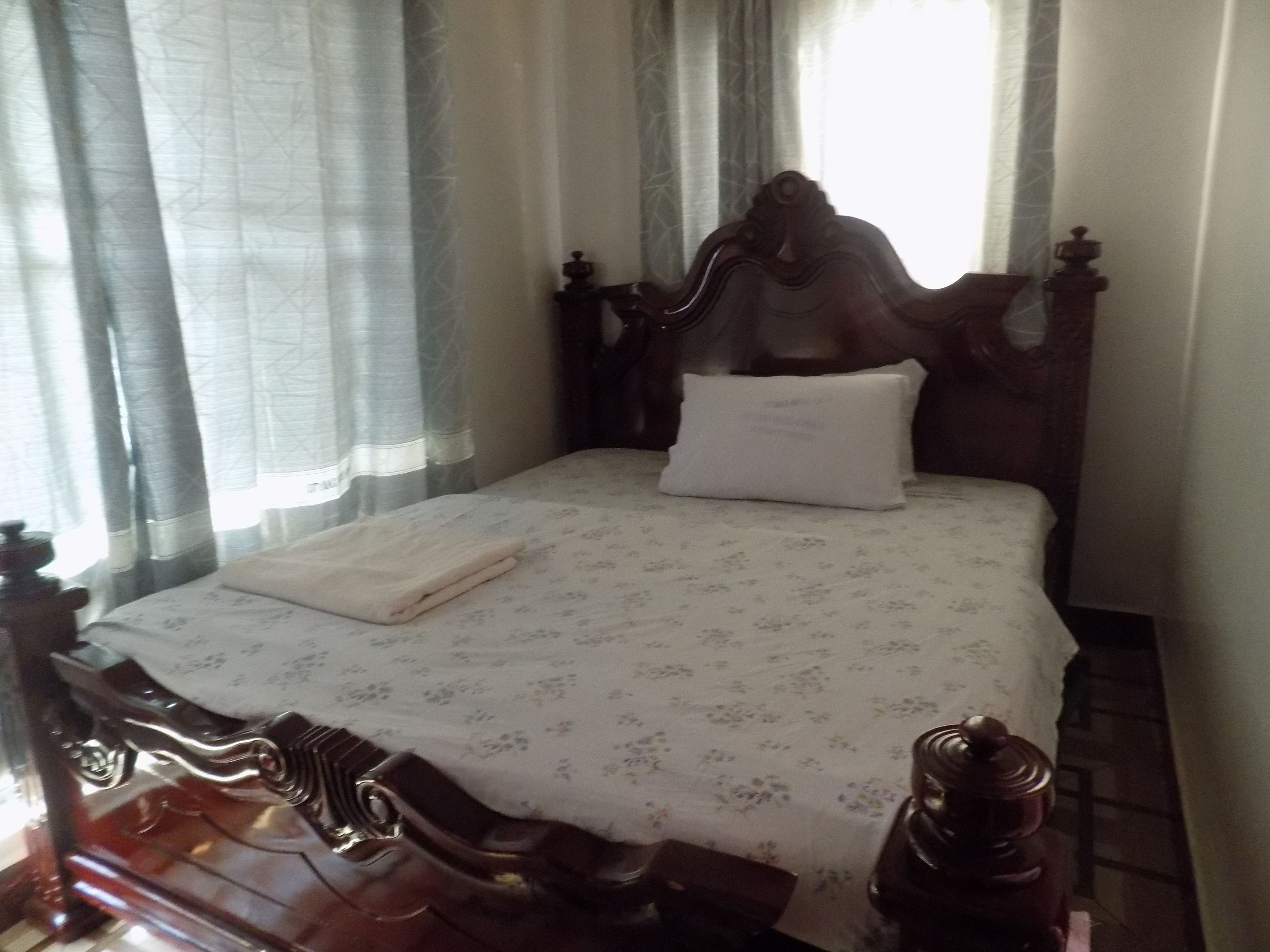 A neatly made bed with a floral bedspread, a white pillow, and a folded towel on a wooden headboard.
