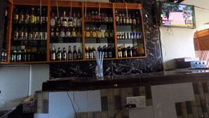 Uma área de bar com prateleiras cheias de garrafas de bebidas, uma televisão na parede e uma tomada na bancada.