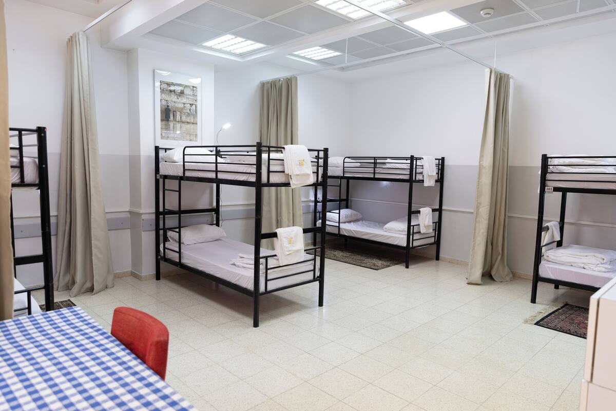 A dormitory room with bunk beds, a checkered table, and a red chair.