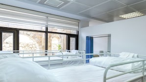 A hospital room with two beds, large windows, and a view of an outdoor stone structure. - New Gate Hostel (Jerusalem)