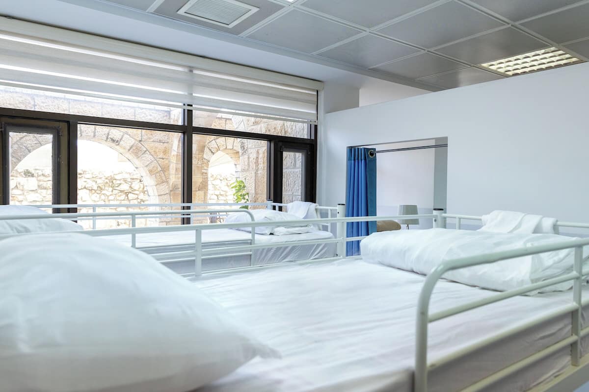 A hospital room with two beds, large windows, and a view of an outdoor stone structure.