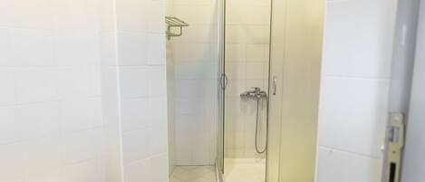 Une salle de bain moderne avec des murs et un sol recouverts de carreaux blancs, une douche à parois de verre et un banc blanc.