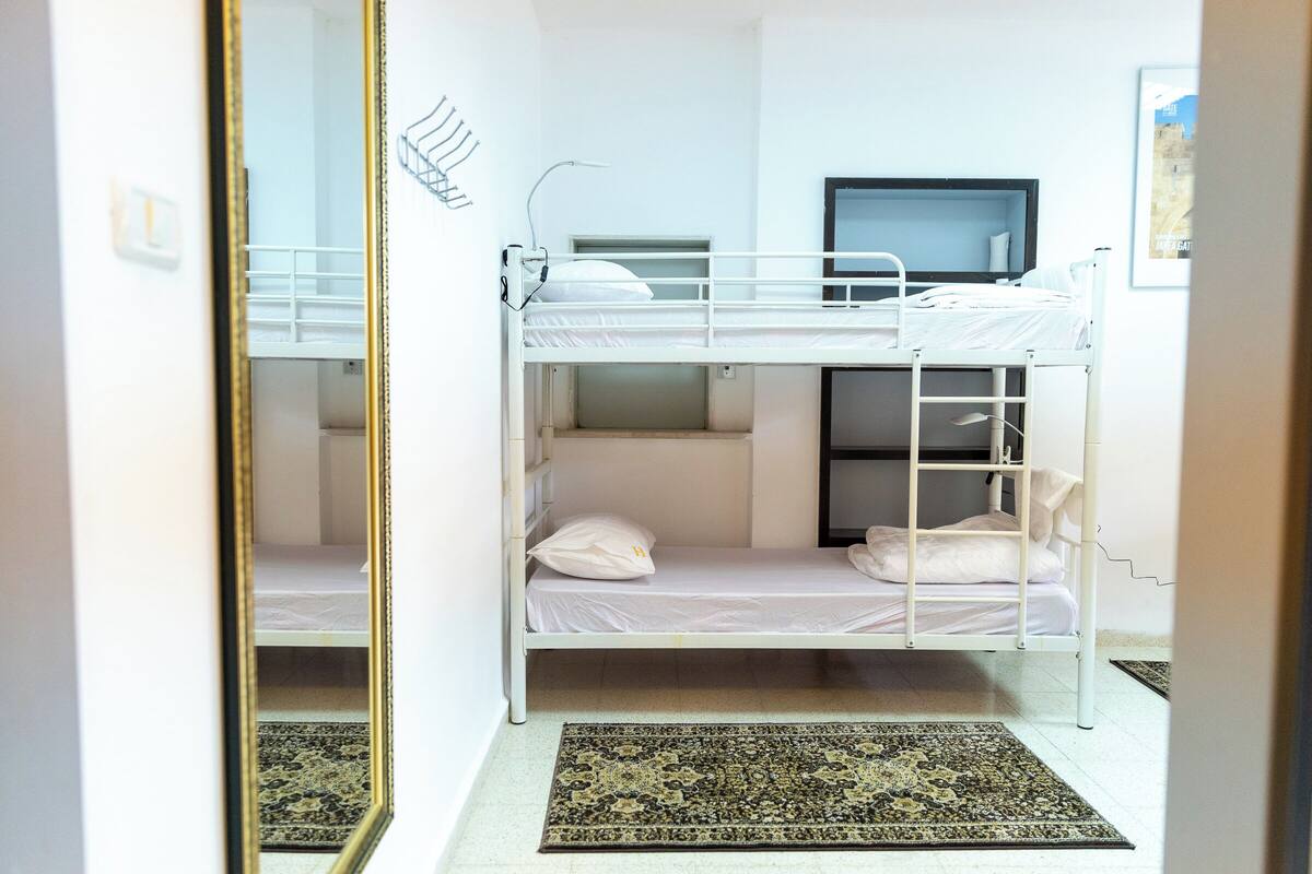 A bunk bed room with a mirror, a small desk, and a patterned rug.