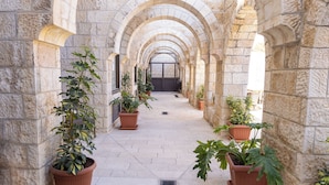 A stone corridor with arches, potted plants, and a drain in the center. - New Gate Hostel (Jerusalem)