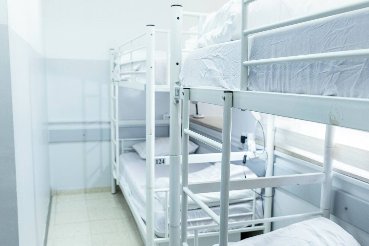 A narrow corridor with bunk beds aligned against the wall, each with a mattress and pillow.
