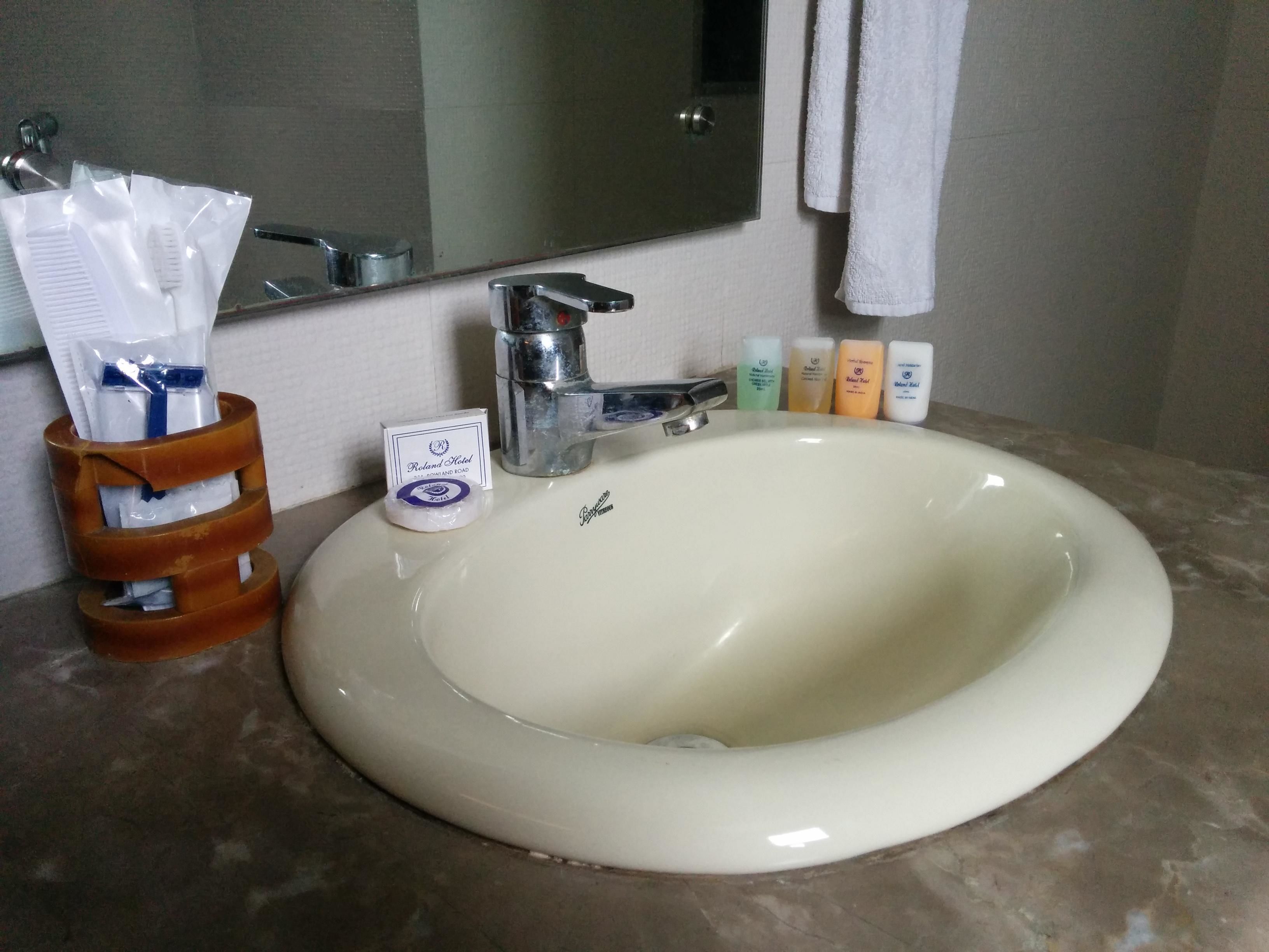 Un lavamanos de baño con un espejo encima, un grifo y artículos de aseo, incluyendo un cepillo de dientes y pasta de dientes.