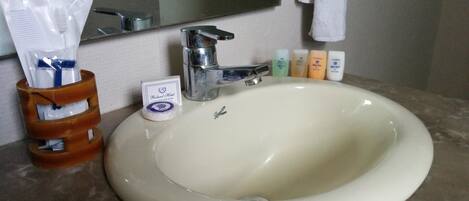 Un lavamanos de baño con un espejo encima, un grifo y artículos de aseo, incluyendo un cepillo de dientes y pasta de dientes.