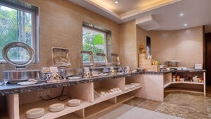 A buffet setup with multiple serving stations, a marble countertop, and a view of the outdoors through large windows. - Roland Hotel (Kolkata)