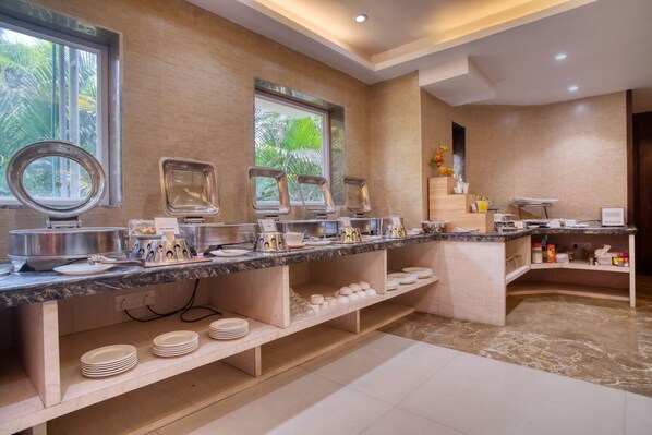 A buffet setup with multiple serving stations, a marble countertop, and a view of the outdoors through large windows.