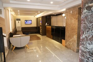 A modern hotel lobby with a reception desk, seating area, and a flat-screen TV.