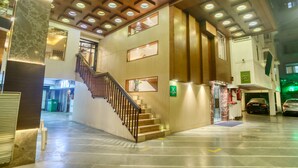 A spacious lobby with a central staircase, a parking area, and a green exit sign. - Roland Hotel (Kolkata)