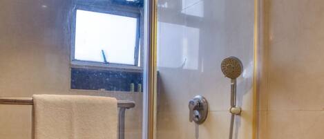 A glass-enclosed shower with a handheld showerhead and a wall-mounted faucet.