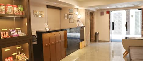 A hotel reception area with a reception desk, a glass display case with snacks, a trash bin, and a sofa.