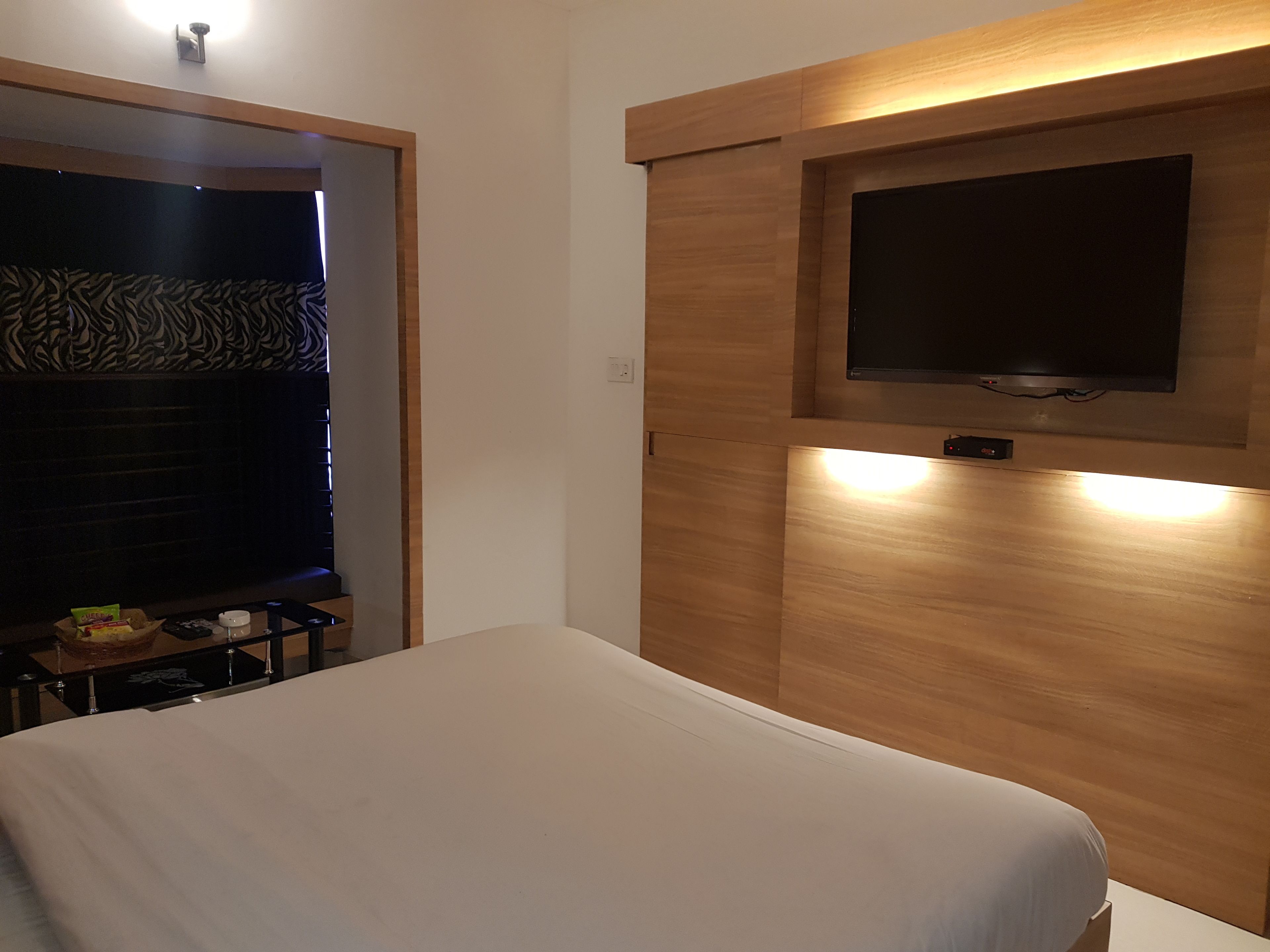 Een hotelkamer met een bed, een aan de muur bevestigde televisie en een kleintje tafeltje met lekkernijen.