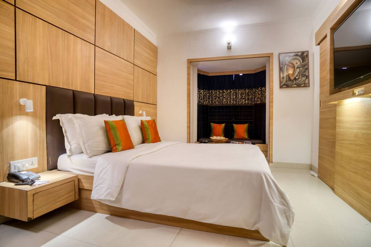Un dormitorio moderno con una cama grande, una mesita de noche, un armario de madera y una zona de estar con cortinas estampadas.