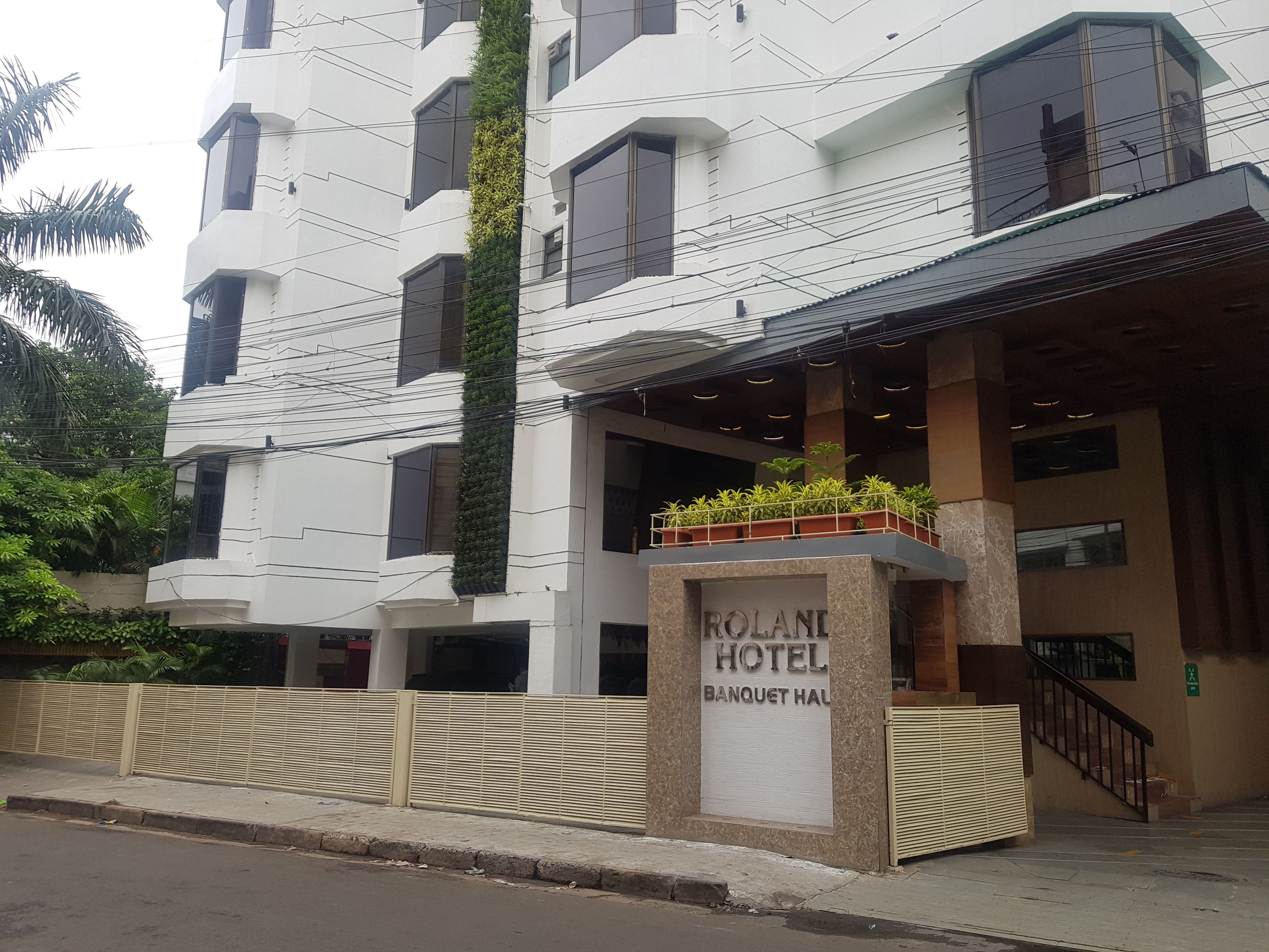 A modern hotel with a white facade, balconies with plants, and a sign for the Rolani Hotel Banquet Hall.