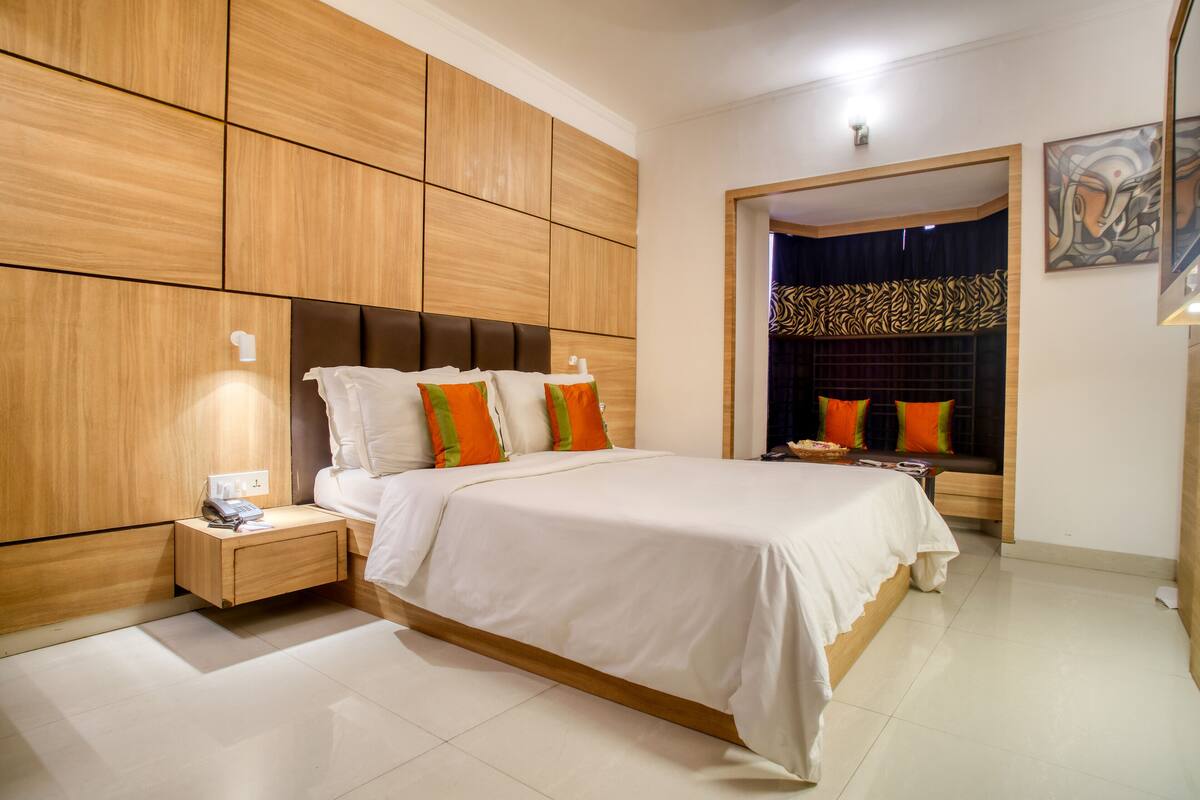 Una habitación de hotel moderna con una cama grande, paneles de madera, una mesita de noche y un detalle decorativo en la pared.
