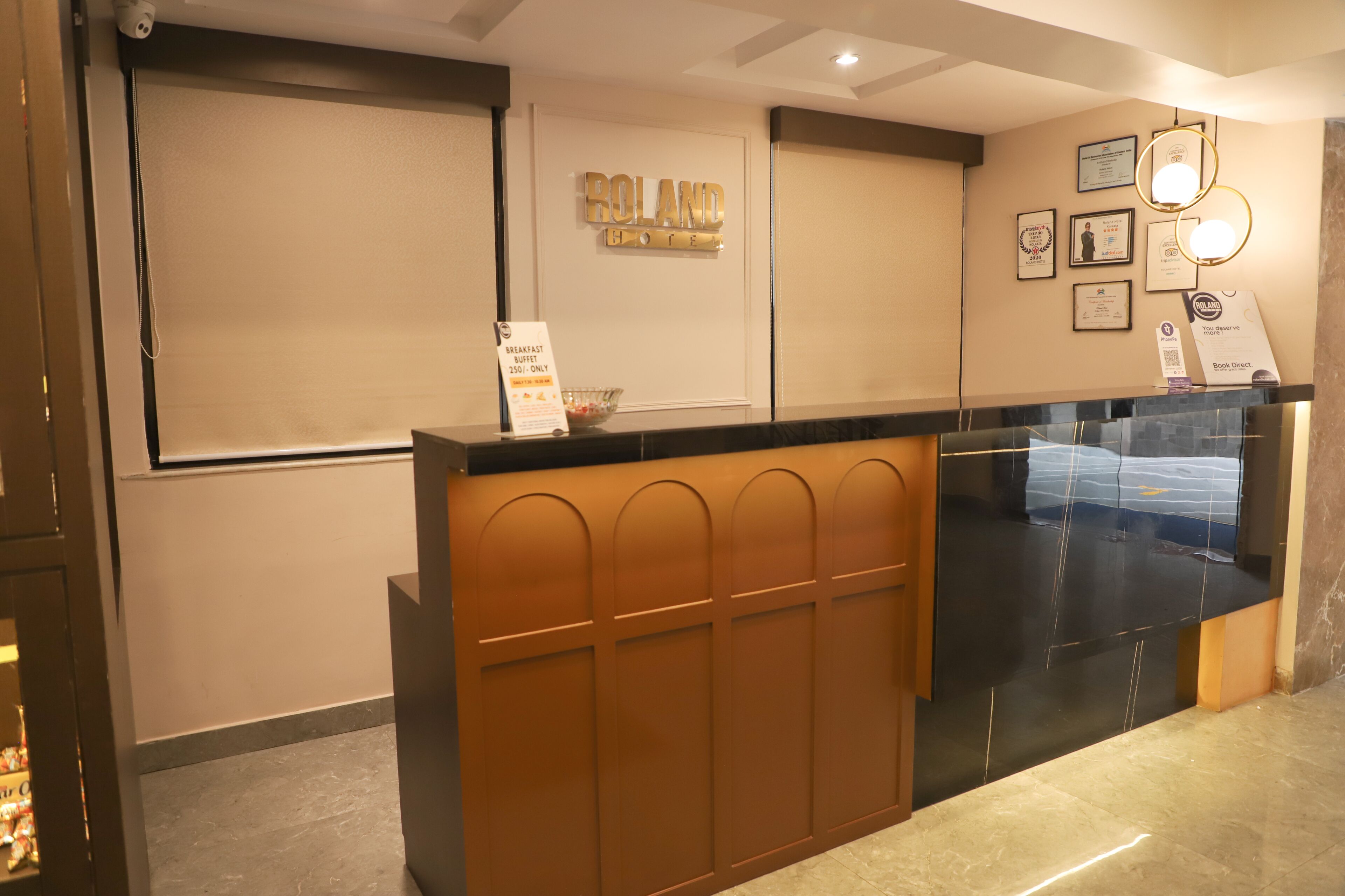 A hotel reception desk with a sign reading "ROLAND HOUSE," a framed certificate on the wall, and a glass display case.