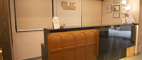 A hotel reception desk with a sign reading "ROLAND HOUSE," a framed certificate on the wall, and a glass display case.
