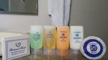 Una encimera de baño con artículos de aseo como gel de ducha, aceite de coco, champú herbal y una pastilla de jabón, junto con un folleto del hotel.