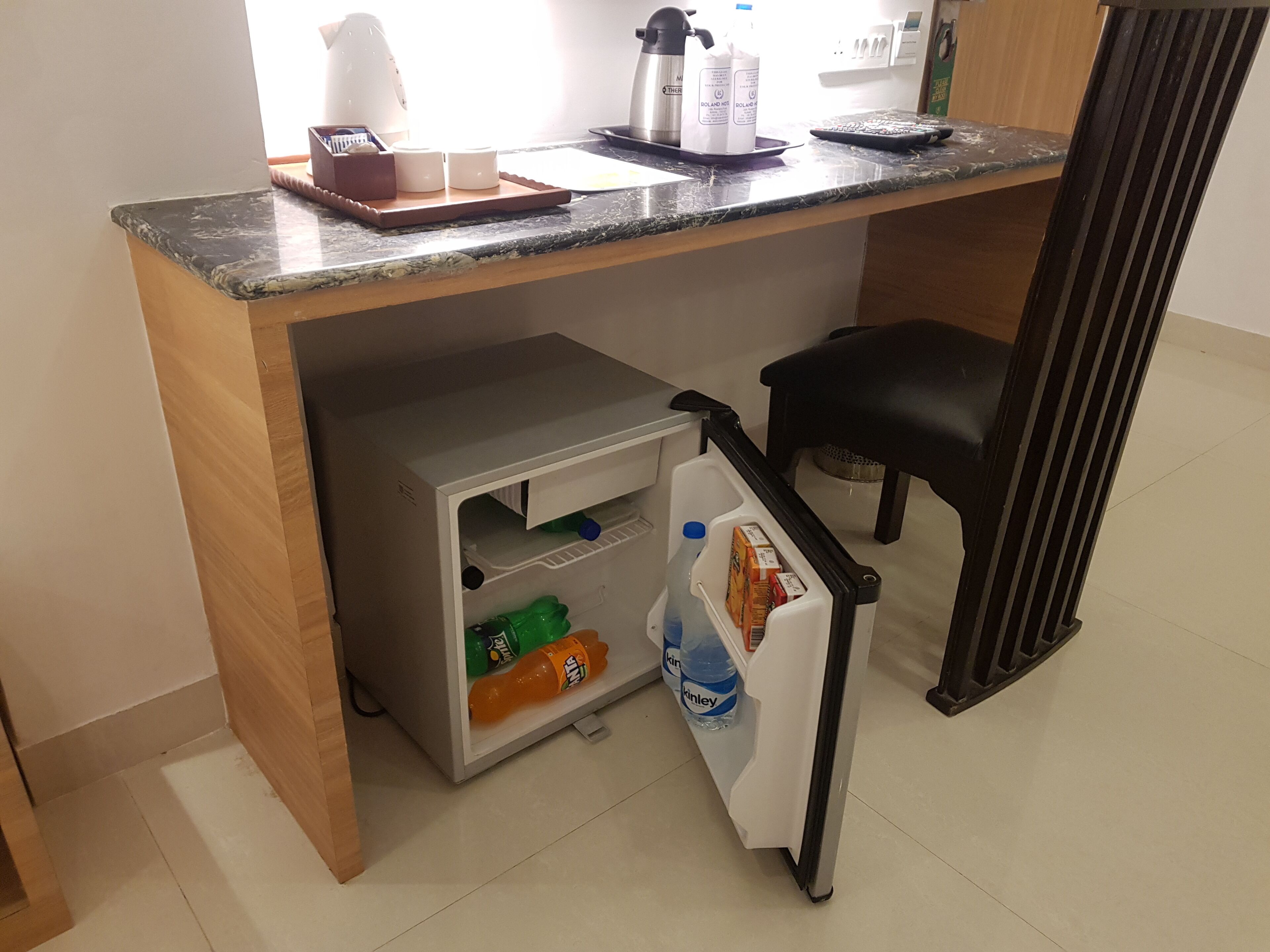 Eine Küchenzeile mit Kühlschrank, Mikrowelle und Kaffeemaschine. Im Kühlschrank befinden sich Wasser- und Limonadenflaschen.