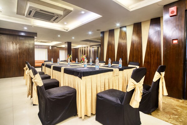 A conference room with a long table, chairs with black covers and beige sashes, water bottles, and a wooden panel wall.