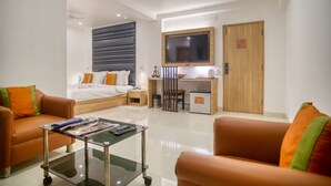 A modern hotel room with a bed, two sofas, a desk, a TV, and a small kitchenette. - Roland Hotel (Kolkata)
