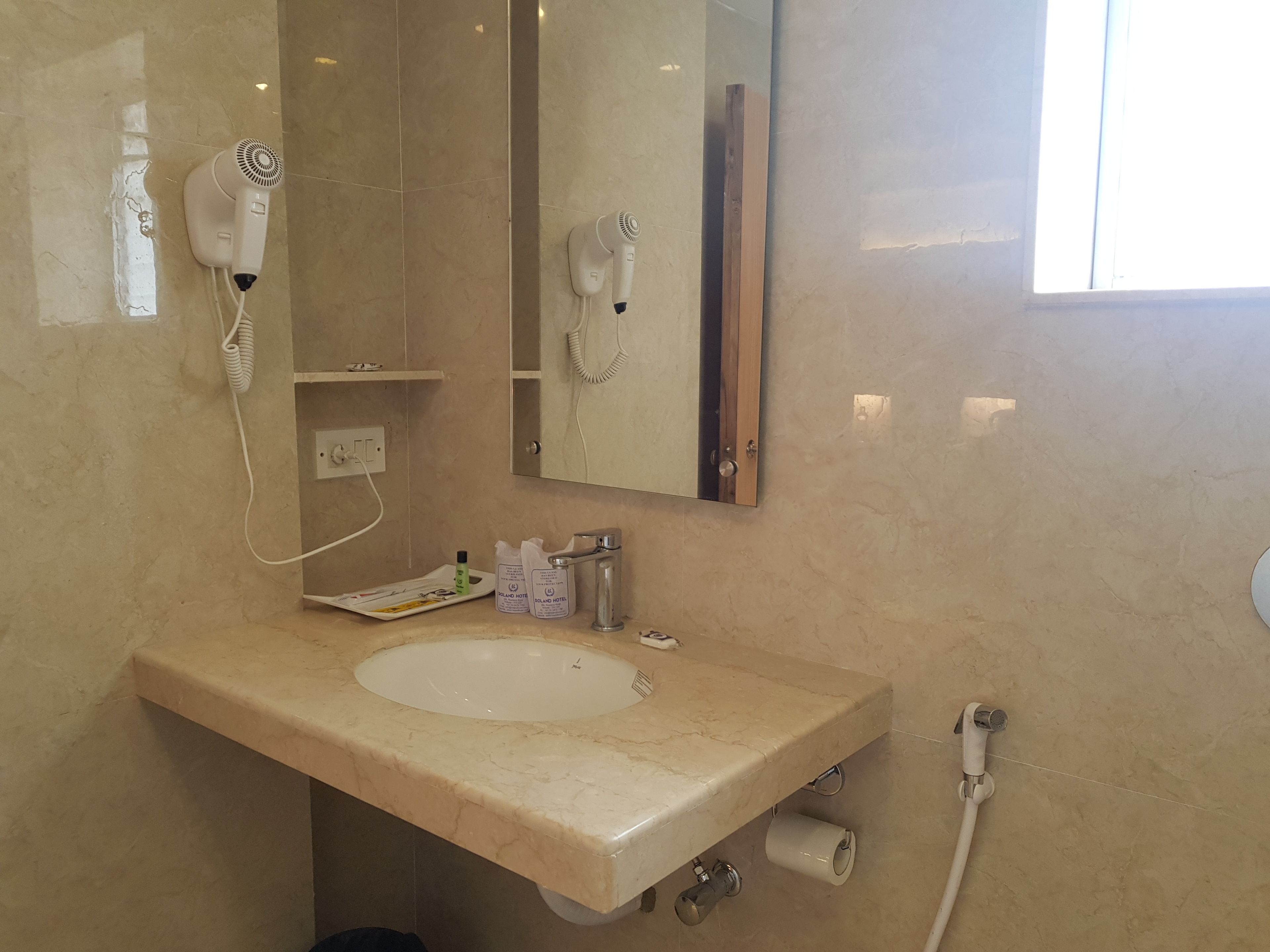 A bathroom with a beige marble sink, a mirror, a hairdryer, a towel rack, and a toilet paper holder.