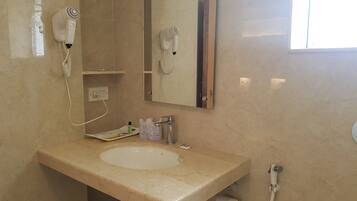 A bathroom with a beige marble sink, a mirror, a hairdryer, a towel rack, and a toilet paper holder.