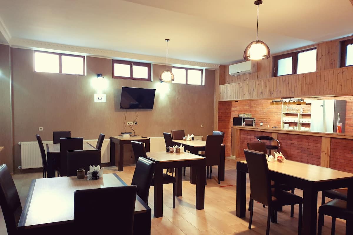 A dining area with wooden tables and chairs, a television mounted on the wall, and a kitchen area with a brick wall and modern appliances.