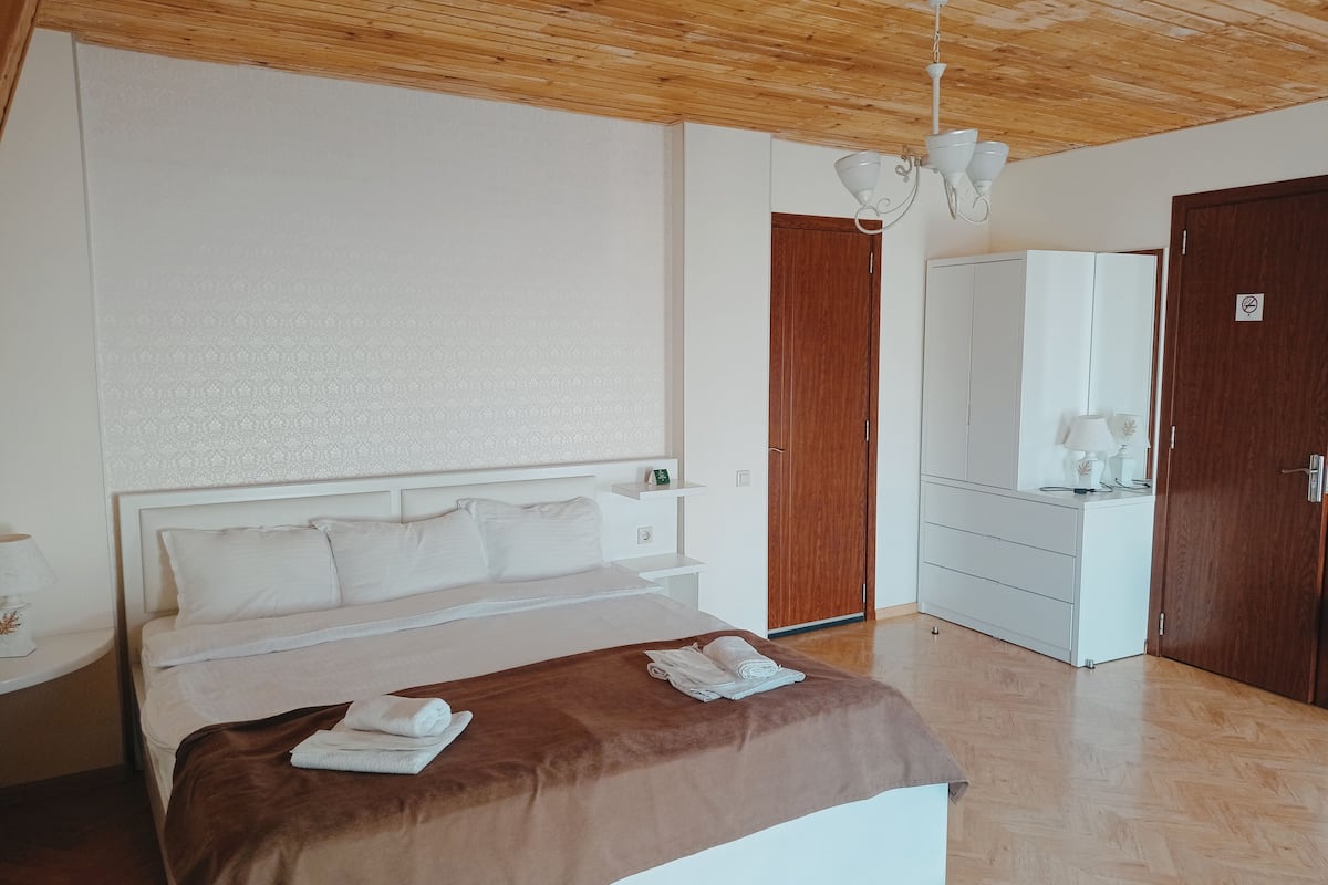 A bedroom with a bed, a wardrobe, a mirror, and a wooden ceiling.
