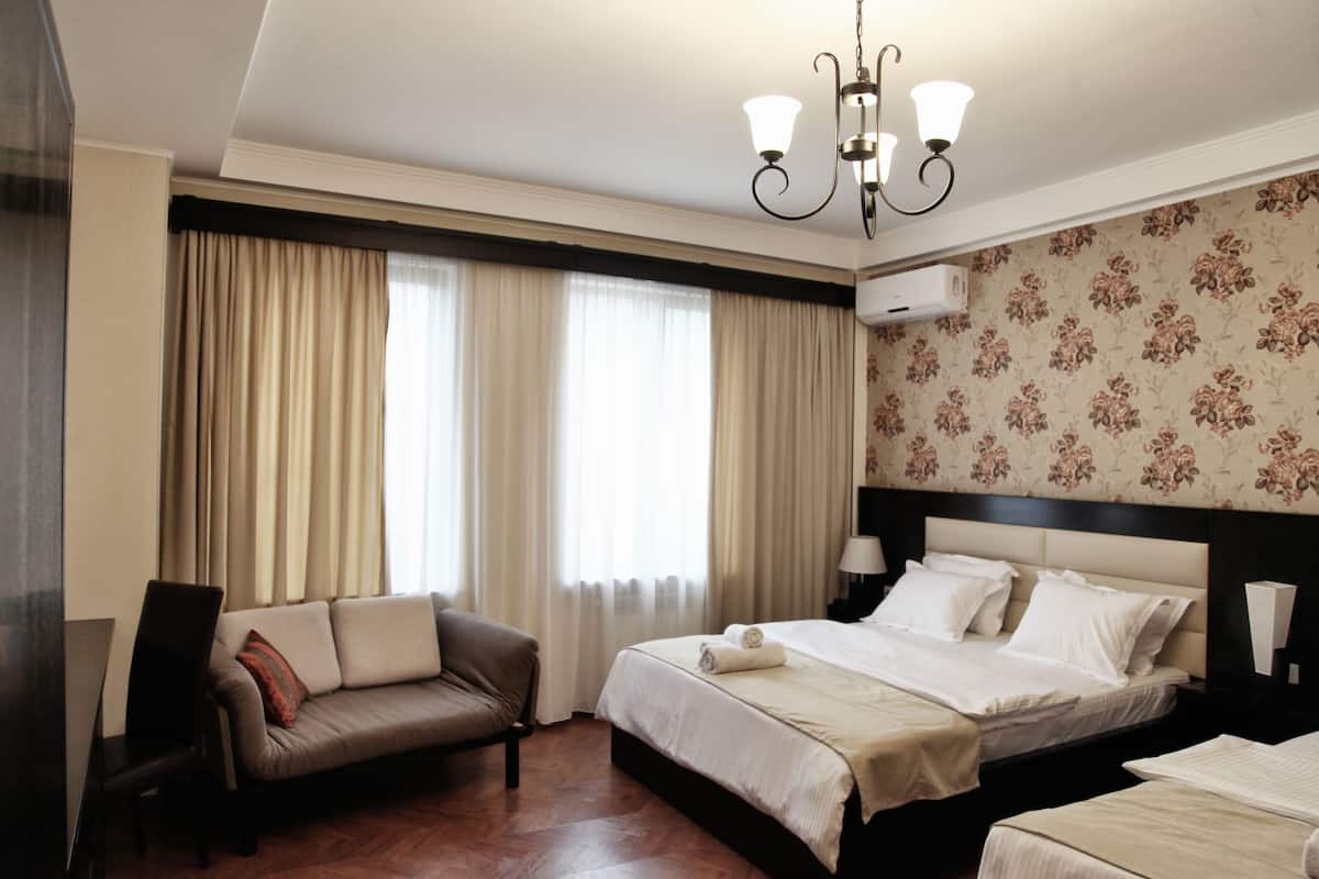A hotel room with a bed, a sofa, a chair, and a large window with curtains.