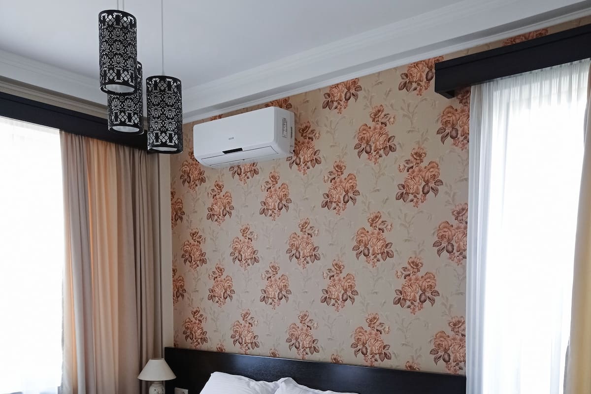 A hotel room with a neatly made bed, a desk, a lamp, and an air conditioning unit on the wall.