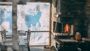 A cozy restaurant with a fireplace, wooden tables, and chairs, and a large window with a mountain view. - Ruka Peak (Kuusamo)