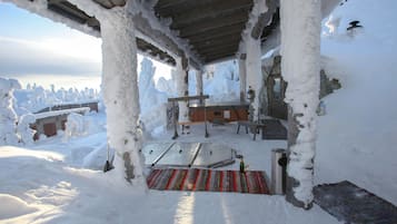 Lumipeitteinen ulkoalue, jossa on puinen penkki ja pöytä. Alueen ympärillä on lumipeitteisiä puita ja kivimuuri.