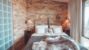 A bedroom with a stone wall, a bed with white linens, two bedside tables with lamps, and a fur throw on the bed. - Ruka Peak (Kuusamo)