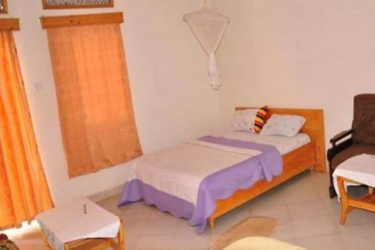 A small, neatly arranged bedroom with a single bed, a small table, and a chair.