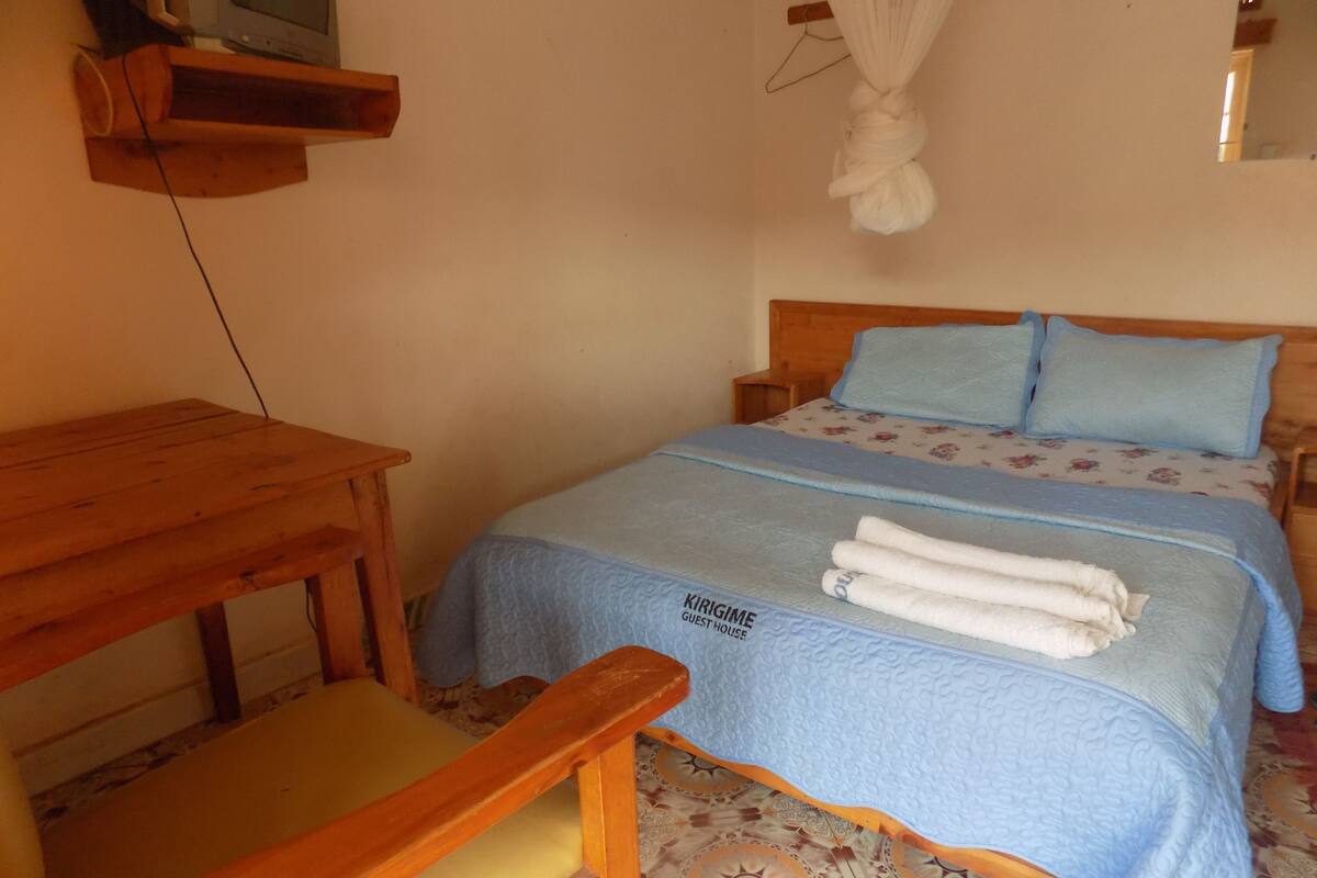 A guest room with a bed, a wooden table, and a television mounted on the wall.