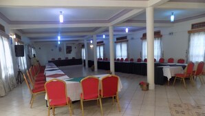 A large hall with rows of tables and chairs, a stage, and a speaker system. - Kirigime Guest House (Kabale)