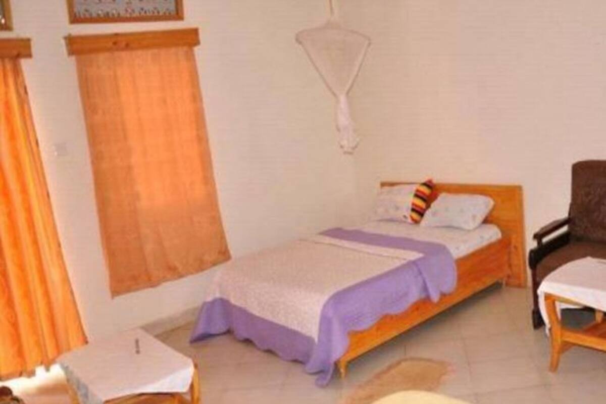 A single bed with a headboard, a bedside table, a chair, and a hanging light fixture.