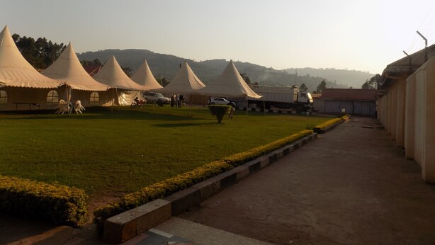 A row of large tents on a grassy field with a paved walkway leading to a building. - Kirigime Guest House (Kabale)