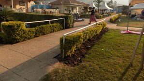 A pathway with manicured hedges, a white railing, and a grassy area with a tent. - Kirigime Guest House (Kabale)