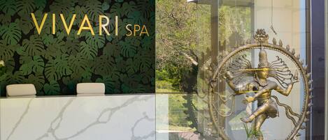 A reception desk with a 'VIVARI SPA' sign, a decorative statue, and a lush green leaf-patterned wall.