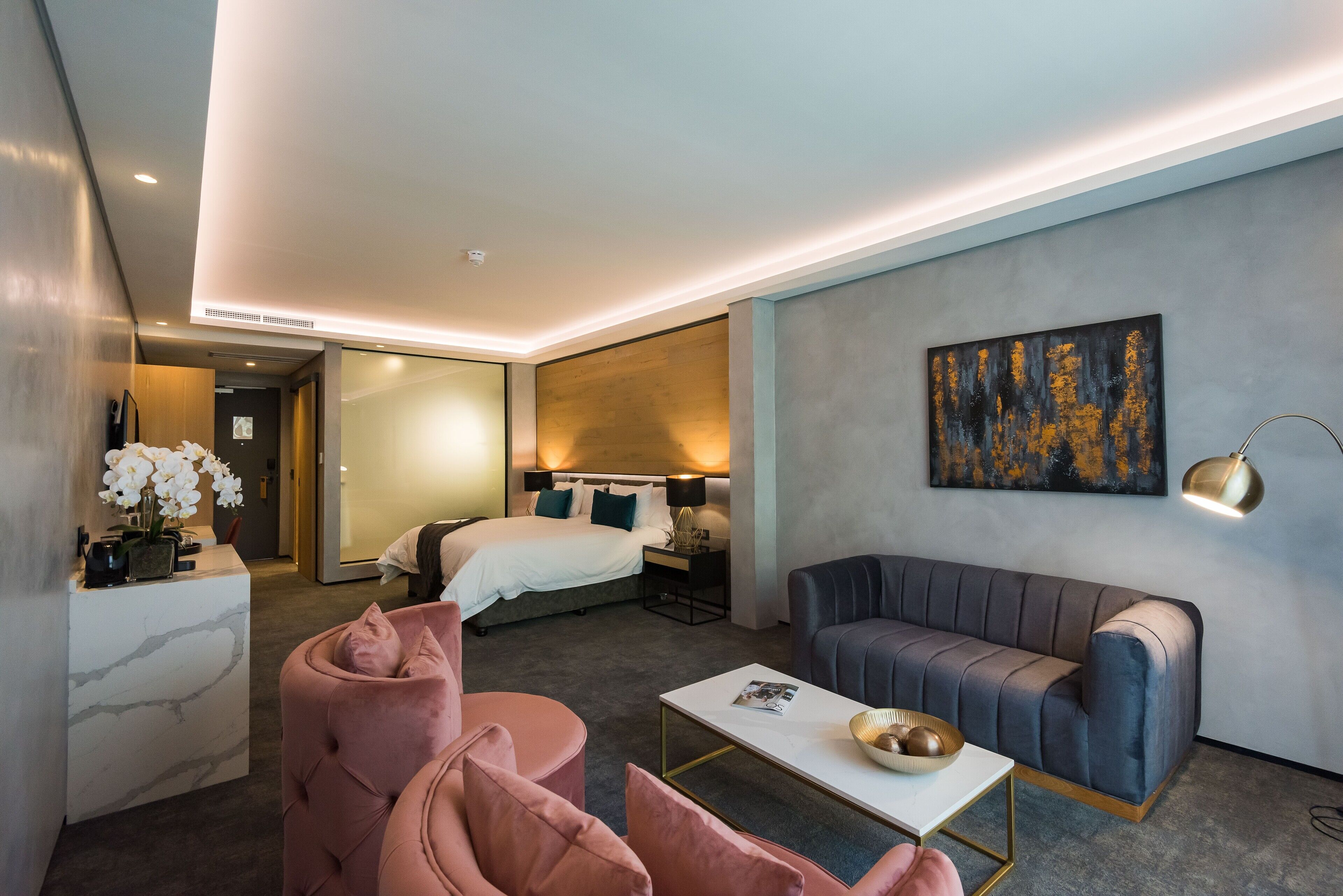 Ein modernes Hotelzimmer mit Bett, einer Couch, einem Couchtisch und einem Schreibtisch mit Blumen.'