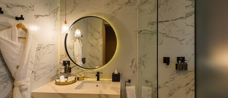A modern bathroom with a marble backsplash, a round mirror, a sink with toiletries, and a towel rack.