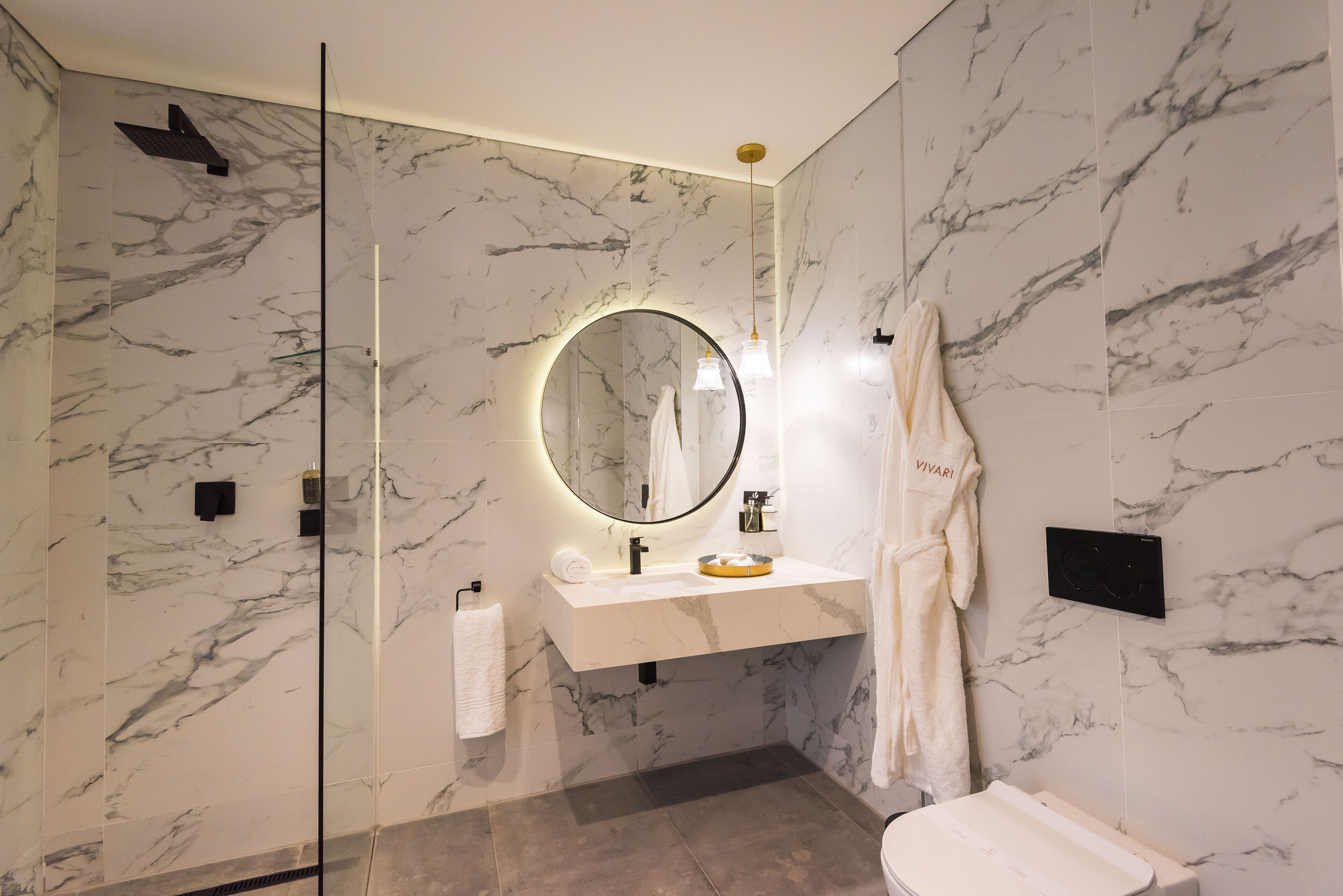 A modern bathroom with a marble wall, a round mirror, a white sink, and a towel rack.